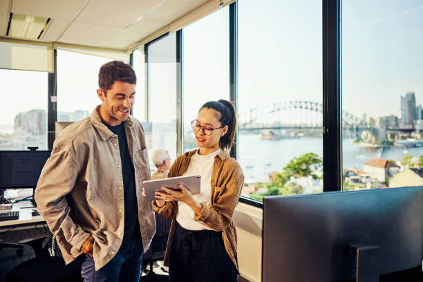 Two people in office with Harbour Bridge through window — collaboration and trust
